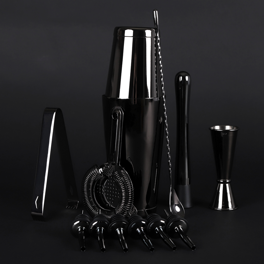 A professional bar tool set in polished black and silver stainless steel, including a shaker, muddler, jigger, strainer, and pourers, arranged on a dark studio background.