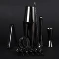 A professional bar tool set in polished black and silver stainless steel, including a shaker, muddler, jigger, strainer, and pourers, arranged on a dark studio background.